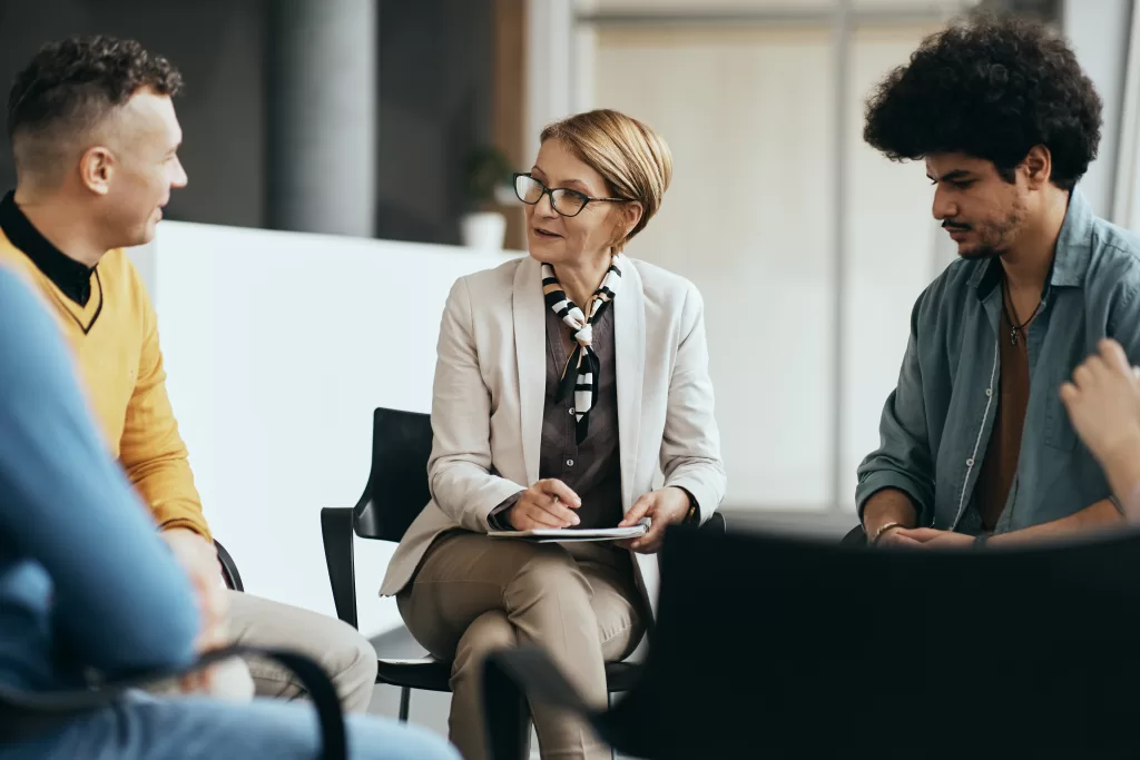 Mature therapist talking to participants of group therapy at mental health center