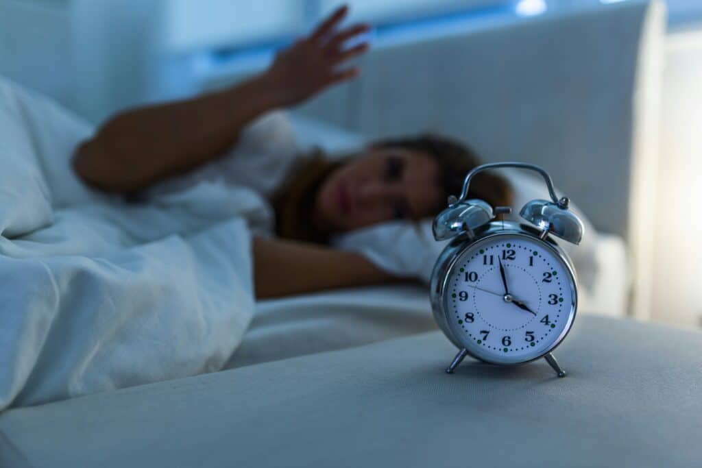 Person lying in bed with an alarm clock, representing insomnia and disrupted sleep patterns at Ventana Mental Health