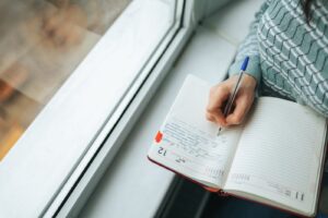 Illustrative stock photo: Person writing in a journal beside a window