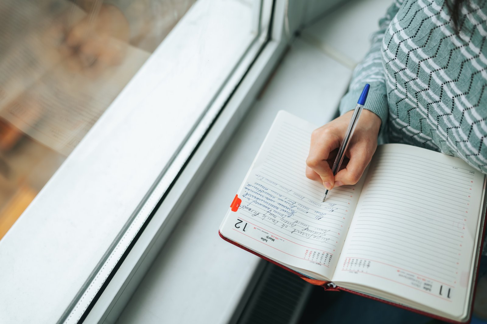 Illustrative stock photo: Person writing in a journal beside a window